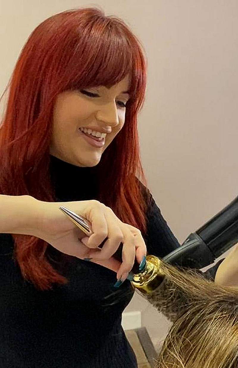 Woman with red hair styling a client's hair in a salon